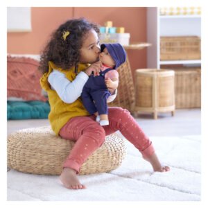 Kleutermeisje kust Corolle babypop in donkerblauwe outfit tijdens het spelen thuis