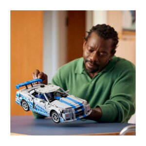 Man bewondert LEGO Technic Nissan Skyline GT-R model in huiselijke omgeving