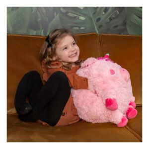 Blij meisje zit op bank met roze unicorn knuffel