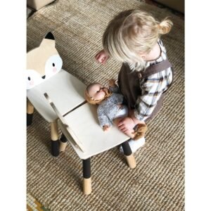 Klein kind speelt met pop op houten vos kinderstoel op vloerkleed