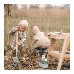 Peuter harkt bladeren met houten kinder tuingereedschap buiten