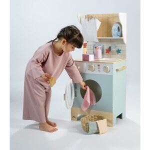Meisje speelt met houten speelgoed wasmachine en haalt wasgoed uit de trommel