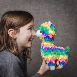 Meisje kijkt lachend naar een kleurrijke regenboog lama knuffel